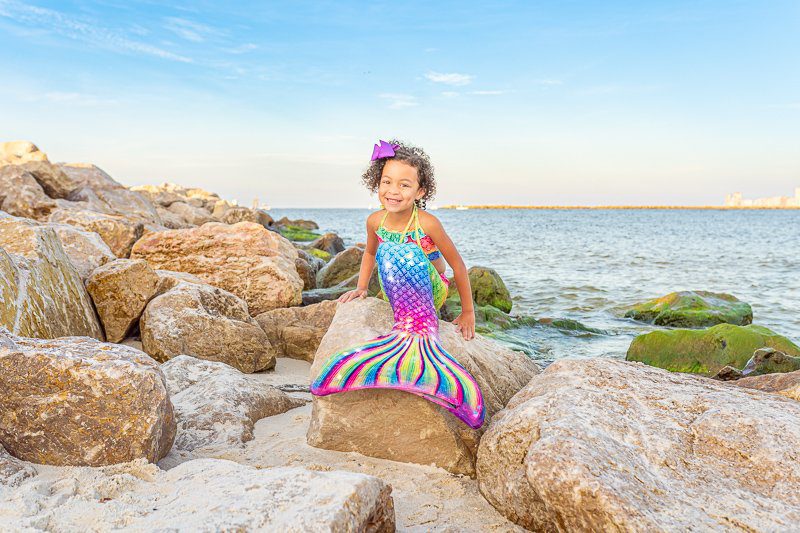 A child dressed as a mermaid, smiling at the camera during a photographers mermaid session in Orange Beach.